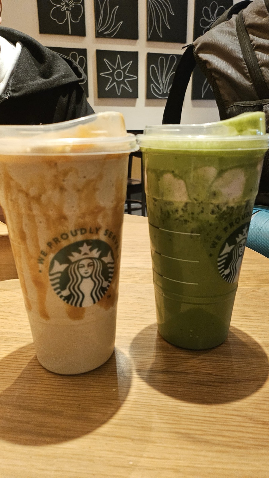 A caramel-topped blended coffee and a bright green matcha drink in clear cups on a wooden table.