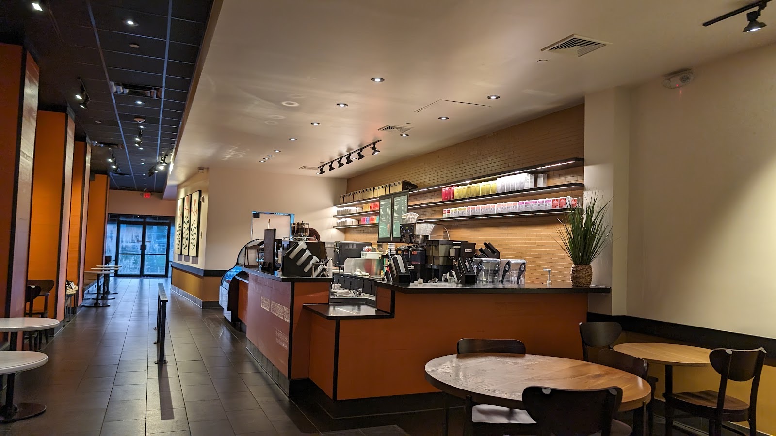 The coffee bar at First Street Coffee: a long counter with lit menu boards, cups and pastries, warm orange walls and small tables.